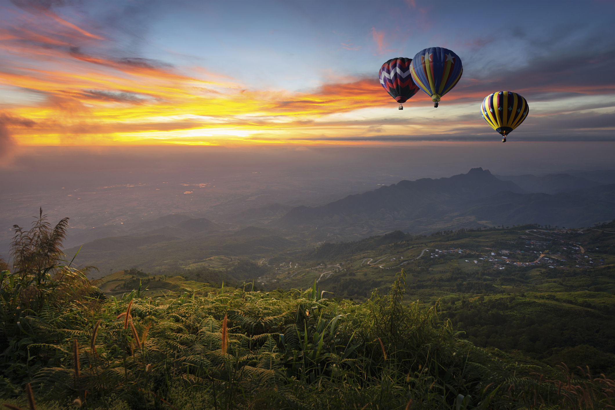 Hot air balloons flying over the mountains with the sunset in the background